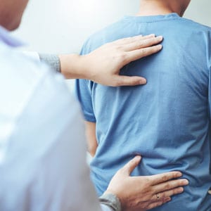 Doctor examines patient's back with hand, assessing for back pain injury - Leep Tescher Helfman and Zanze