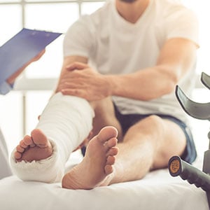 A man with a broken leg sitting on a bed, wearing a cast - Leep Tescher Helfman and Zanze