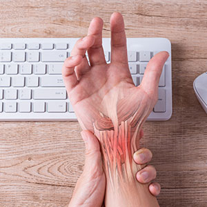 Person holding wrist in pain, hand resting on computer keyboard symbolizing Workplace Injury - Leep Tescher Helfman and Zanze