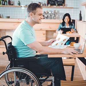 A man in a wheelchair using a laptop at a table representing Disability - Leep Tescher Helfman and Zanze