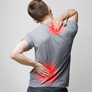 A person in discomfort holds their lower back, red glow highlighting spinal pain. - Leep Tescher Helfman and Zanze