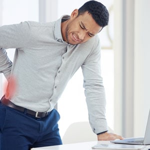 A man with hand on his back - Back pain at the workplace - Leep Tescher Helfman and Zanze