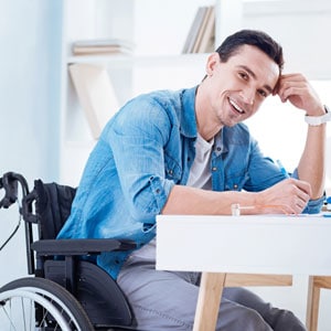 A man in a wheelchair sits at a desk with a laptop, symbolizing returning to his job after a work-related injury. - Leep Tescher Helfman and Zanze