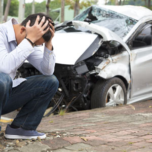 A man sitting on the ground next to a damaged car after a car accident - Leep Tescher Helfman and Zanze
