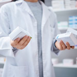 A pharmacist in a white coat holding a medicine box in a pharmacy. - Leep Tescher Helfman and Zanze